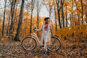 Young woman in classic trench coat with retro bicycle in yellow autumn park. Amazing scene of trendy girl on nature background. Environmentally friendly mode of transport