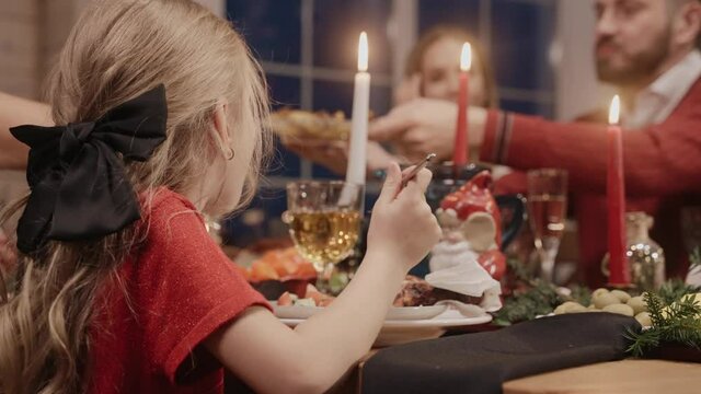 Little girl eating at the dining table on Christmas Eve, dressed up in red. Family gathering for Christmas celebration. High quality 4k footage