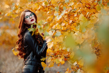 portrait of a beautiful young woman, wearing stylish glasses, looking at the camera. Happy, confident, smart young woman in autumn foliage