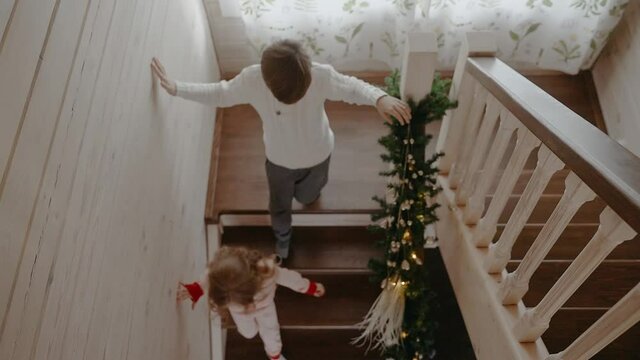 Excited boy and girl are running down the stairs on Christmas morning. Christmas morning in big and bright house. Kids are excited to get their presents. 50 fps