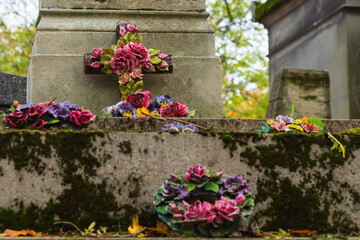 Fototapeta na wymiar Cemetery in autumn . Grief and memorial. Flower decorated ceramic cross and wreaths over tomb. Mourning vintage background. Funeral services retro design concept. Selective focus on cross.