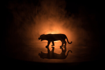 Fototapeta premium A silhouette of lion miniature standing on wooden table. Creative decoration with colorful backlight with fog. Selective focus