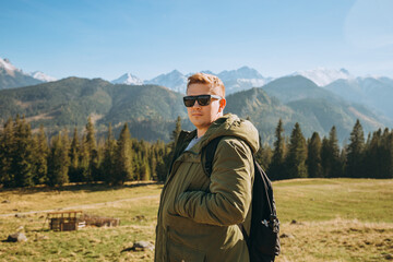 Young man in sunglasses see view on top mountain. Freedom, happiness, travel and vacations concept, outdoor activities