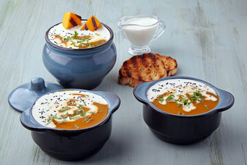 Creamy pumpkin soup in bowls and pot with cream,
