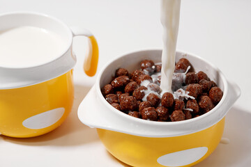 Pours milk into a children's bowl with ready-made breakfast