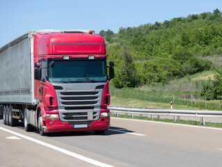 Fototapeta na wymiar Red Semi-trailer driving along highway. Goods Delivery by roads. Services and Transport logistics
