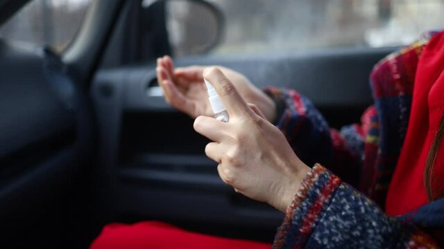 An Asian woman sitting in car seat. spraying antibacterial sanitizer spray on hand in car.