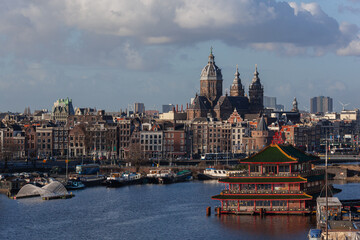Obraz premium Scenic Amsterdam harbor with boats, ships and famous floating Chinese restaurant against the backgound of historical church and panoramic city view, Netherlands.