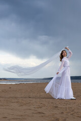 Happy young girl in a white dress on the river bank. Stormy sky in the clouds
