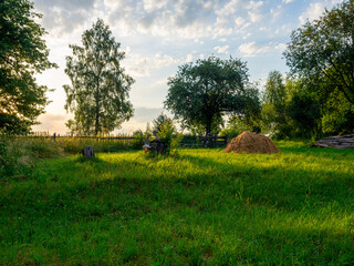 Fototapeta premium Summer rural landscape. Green glade, yellow village stack, old wooden fence