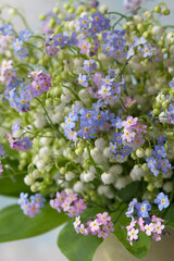 Bouquet of spring flowers of lilies of the valley, blue and pink forget-me-nots close-up on a decorative light background. Blur, selective focus.