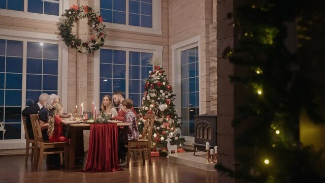Whole family talking and eating at the table on Christmas Eve, filmed from afar. Family gathering for Christmas celebration. 50fps. High quality 4k footage