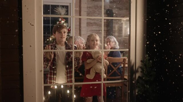 Boy and girl are looking out of the window, excited about snow on Christmas Eve. Christmas Eve in big and bright house. Kids are excited t o see snow on Christmas. 50 fps