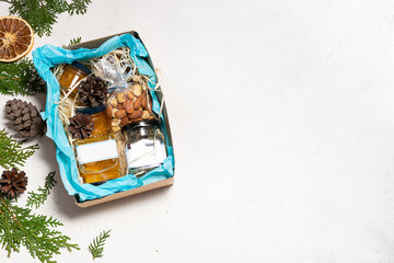 Healthy zero waste Christmas gift idea. Set of organic jams, honey, nuts and tea in the box with natural festive decorations on white stone background. COpy spce for your design.