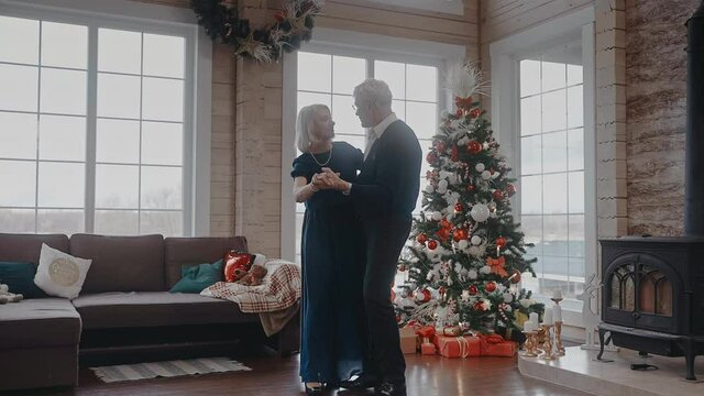 Grandparents dancing together at the Christmas celebration near the fireplace and tree. Active grandad spinning and dancing waltz with grandmother against Christmas tree. 50fps. 4k footage