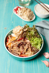 Korean cuisine. Crystal noodles with beef, vegetables and mushrooms. Close-up, on a blue wooden background, vertical