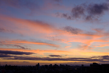 都市の夜明け。雲がオレンジ色に染まりビルぐんがシルエットに浮かぶ