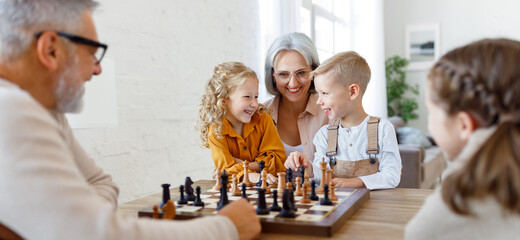 Children brother and sister playing chess while sitting in living room with senior grandparents