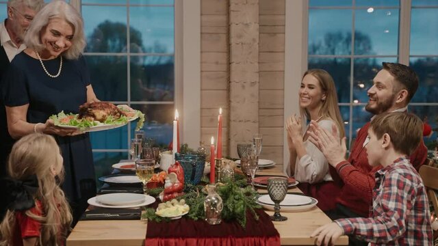 Grandmother serves chicken on the table on Christmas Eve, everybody clapping. Family gathering for Christmas celebration. 50fps. High quality 4k footage