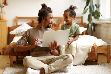 Happy african american family little son with dad watching funny videos on laptop together at home