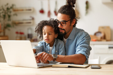 Young african american dad helping schoolboy son with homework on laptop during distant education