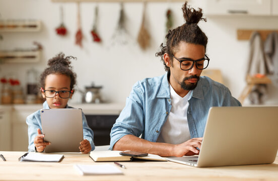 African american father and son using gadgets laptop and tablet while sitting at desk at home