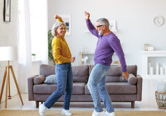 Energetic senior family couple dancing together in living room at home, moving to music