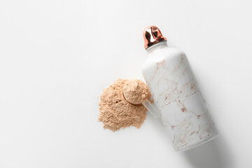 Bottle with protein shake and scoop with powder on white background