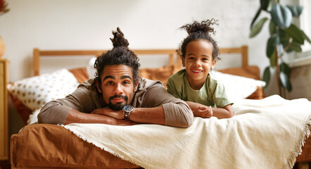 Happy african american family father and son little boy lying and relaxing on bed