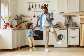 Happy african american family father and little son dancing to music in modern kitchen at home - Powered by Adobe