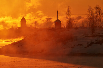 Blazing morning sunrise behind small beacon or lighthouse on the rocky island in front of Suomenlinna fortress island on an extremely cold winter morning at sunrise.