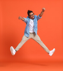 Full length shot of young emotional overjoyed african american man jumping over orange background