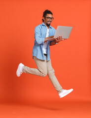 Young happy overjoyed african american man with laptop computer jumping over orange background