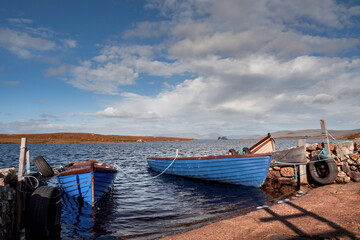 Fishing boats by a small pier on a lake with blue water in Connemara, county Galway, Ireland. Hobby and active sport concept. Nobody. Beautiful Irish landscape. Warm and blue colors. Cloudy sky.