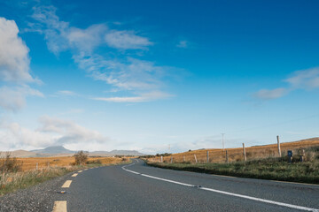 Fototapeta na wymiar Small asphalt road, Croagh Patrick mountain on the left, Beautiful rich blue cloudy sky. County Mayo, Ireland. Travel and transportation. Low angle shot.