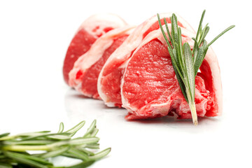 Three fresh uncooked lamb chops with bone in on a white isolated surface with rosemary herb. Selective focus. Meat industry production product and butcher craft example.