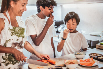 two brothers of Asian and Indian origin, cooking with their mother, tasting a carrot. healthy,...