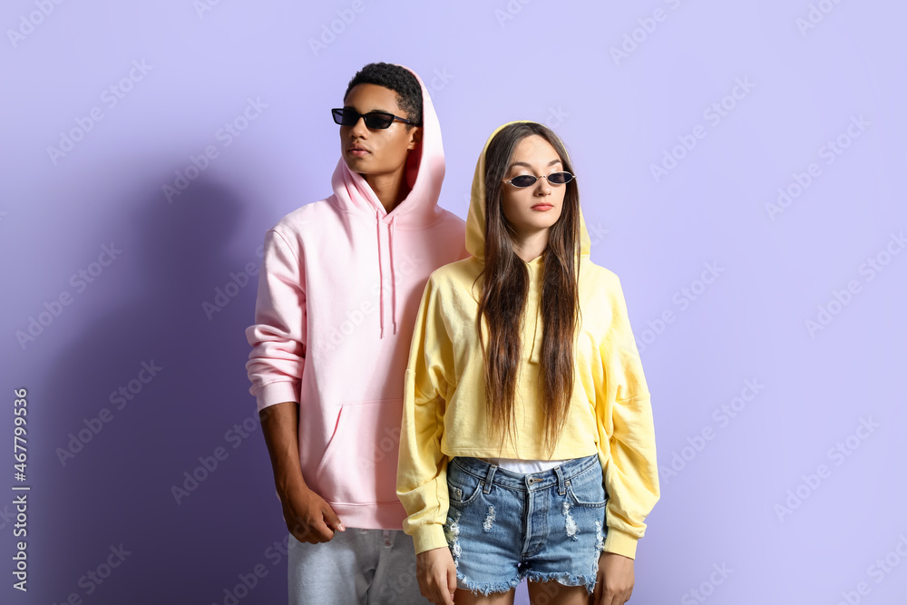 Wall mural Stylish young couple in hoodies on violet background - Wall murals