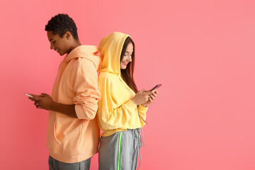 Stylish young couple in hoodies using mobile phones on pink background