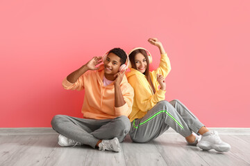 Fototapeta na wymiar Stylish young couple in hoodies with headphones near pink wall