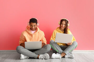 Stylish young couple in hoodies using laptops near pink wall