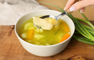 Woman eating tasty dumpling soup at table, closeup