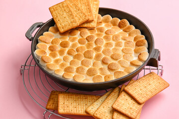 Frying pan with tasty S'mores dip and crackers on pink background