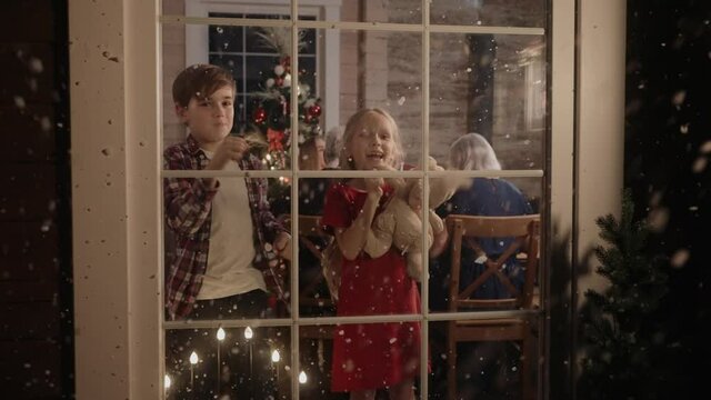 Boy and girl are looking out of the window, excited about snow on Christmas Eve. Christmas Eve in big and bright house. Kids are excited t o see snow on Christmas. 