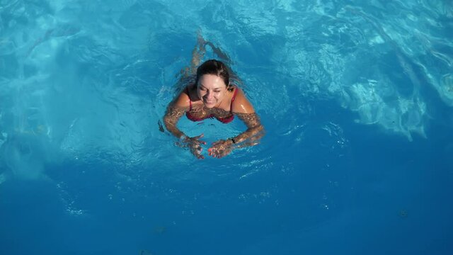 Happy woman smiling and swimming breastroke in a swimming pool with blue water