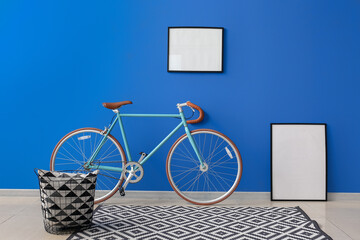 Bicycle, blank frames and basket with pillow near bright blue wall