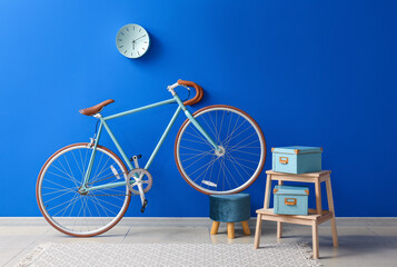 Bicycle with pouf, stepladder and boxes near bright blue wall