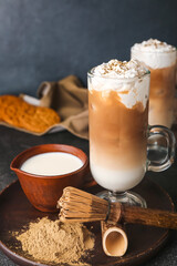 Glass cups of iced hojicha latte, chasen and powder on black background