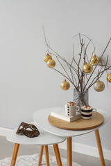 Christmas decoration with tree branches and golden balls in vase on coffee table near grey wall