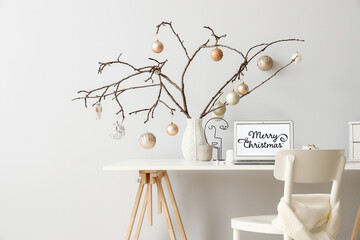 Festive workplace with Christmas decoration and tree branches with different balls on light wall background